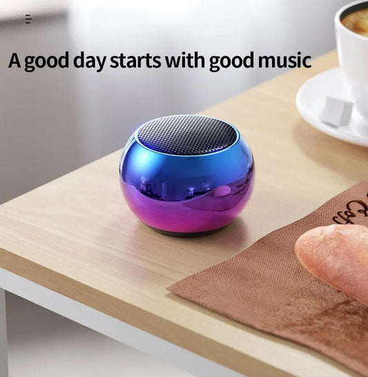 Small blue and purple portable speaker on a wooden surface with text 'A good day starts with good music'.